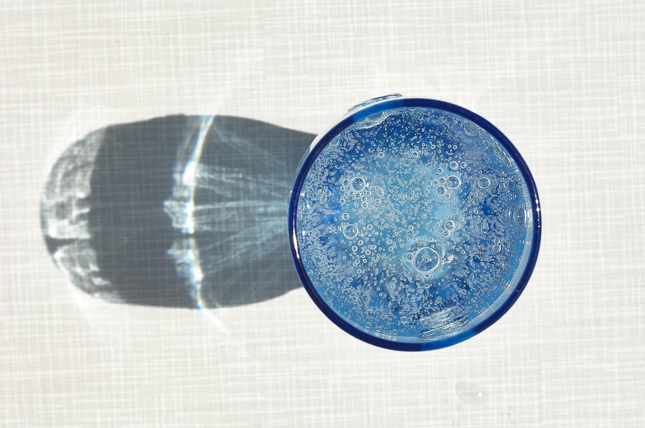 Donna che beve acqua da un bicchiere, illustrando l'importanza dell'idratazione corretta.