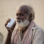Uomo che guarda preoccupato un bicchiere d'acqua, segnale di scarsa idratazione.