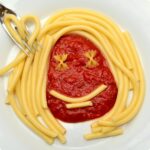Pasta al pomodoro servita in un piatto, decorata con basilico fresco e olio d'oliva.
