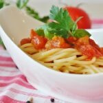 Pasta al pomodoro servita in un piatto, con ingredienti freschi sullo sfondo.