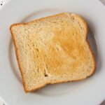 Fette biscottate su un tavolo, con un caffè e un libro aperto, simbolo di una merenda pomeridiana.