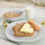 Fette biscottate integrali servite a colazione con burro e marmellata su un tavolo.